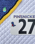 pinsnickety cactus pin on a fly bonnet and t-rex horse pin on a horse show number attached to a saddle pad