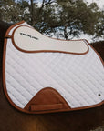 Brown and white saddle pad on a horse with trees in the background